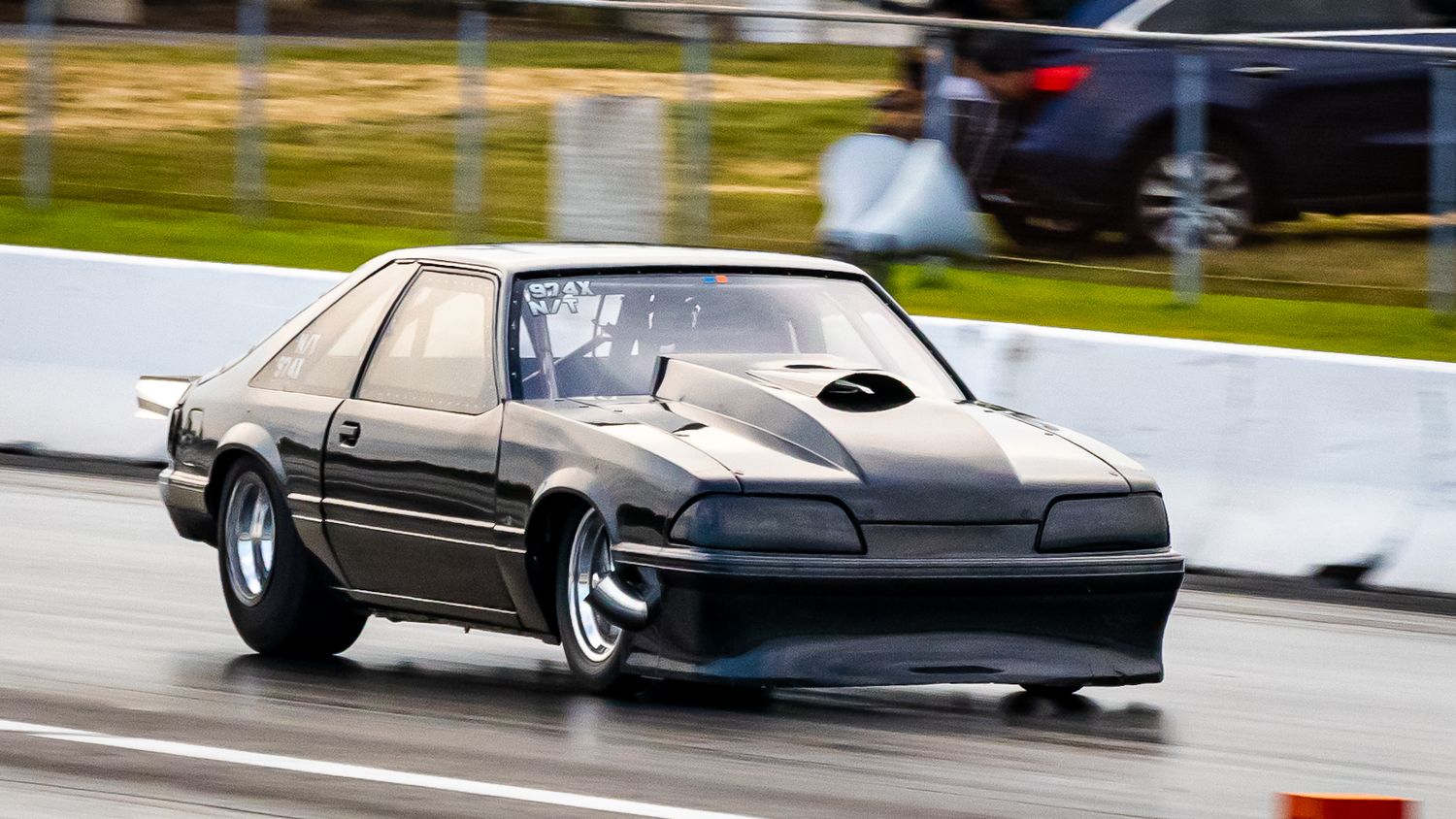 Gold and black race cars line up at a drag strip on a cloudy day.