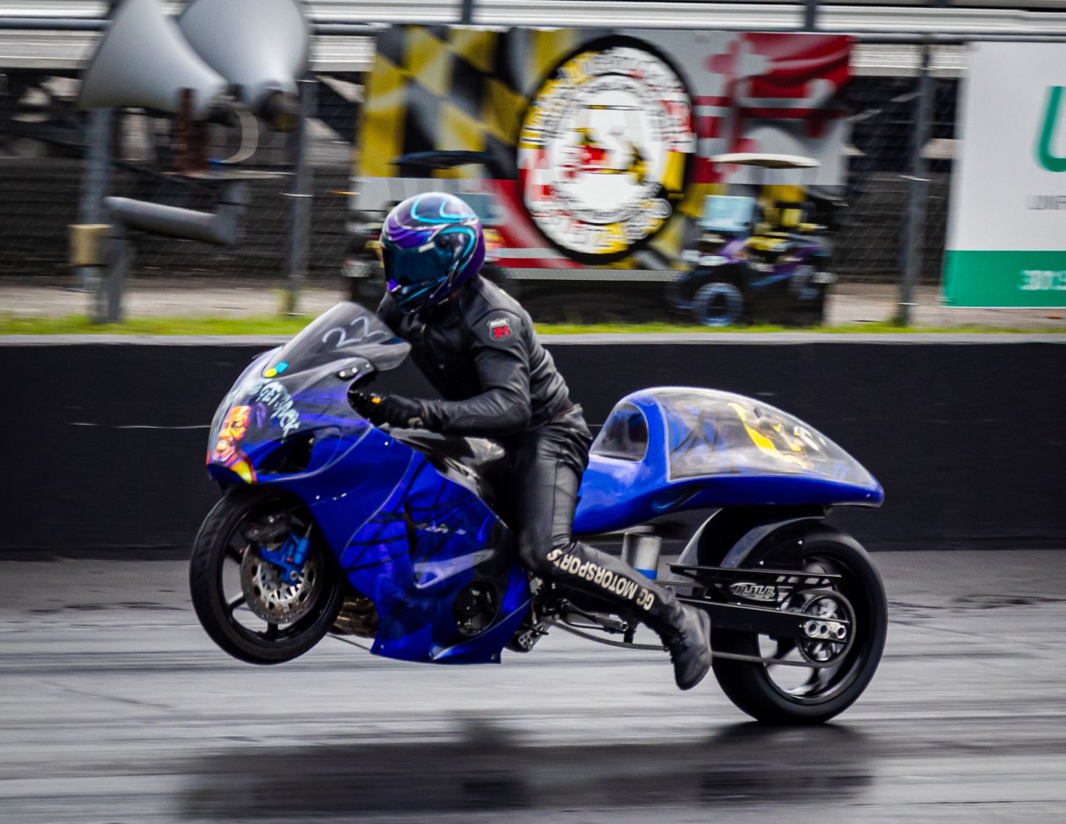 Blue motorcycle drag racer speeds down track with motion blur effect.