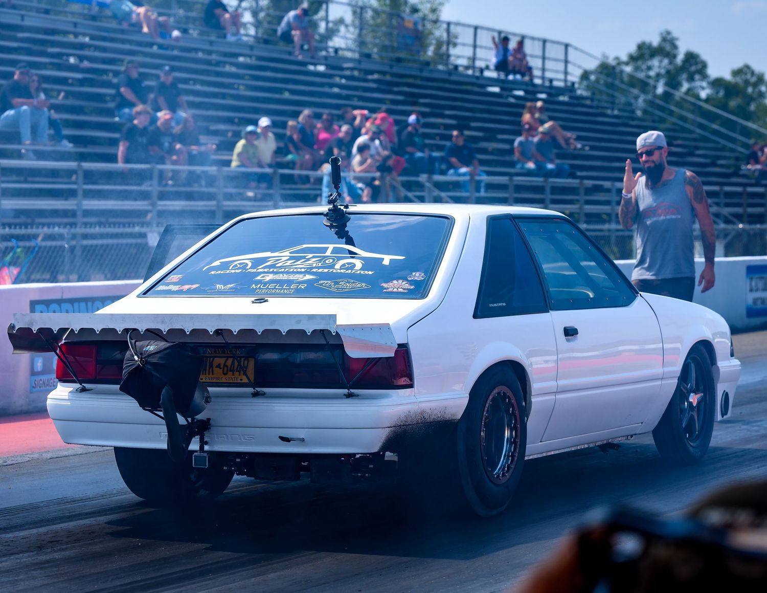 White sports car racing down a drag strip at night with illuminated track lights visible in the background.