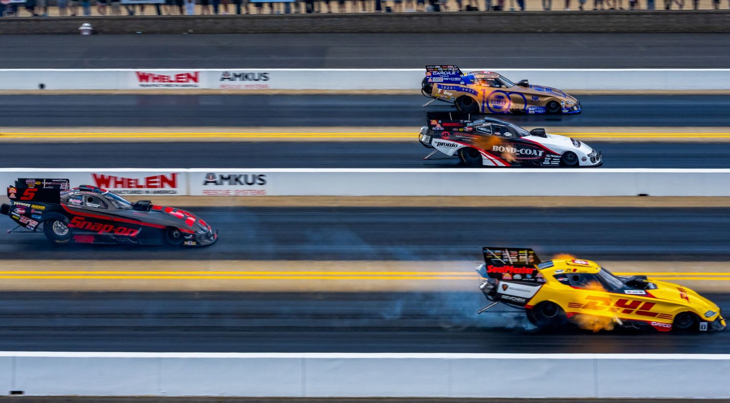 Multiple drag racing vehicles competing on professional track with spectators in background.