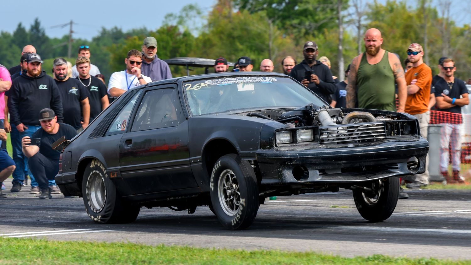 Spectators watch classic cars compete at a drag racing event.