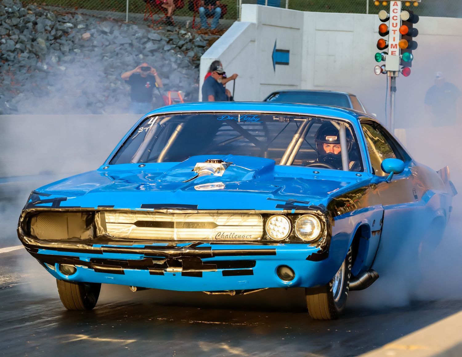 A bright blue drag racing car doing a burnout at the starting line with smoke billowing.