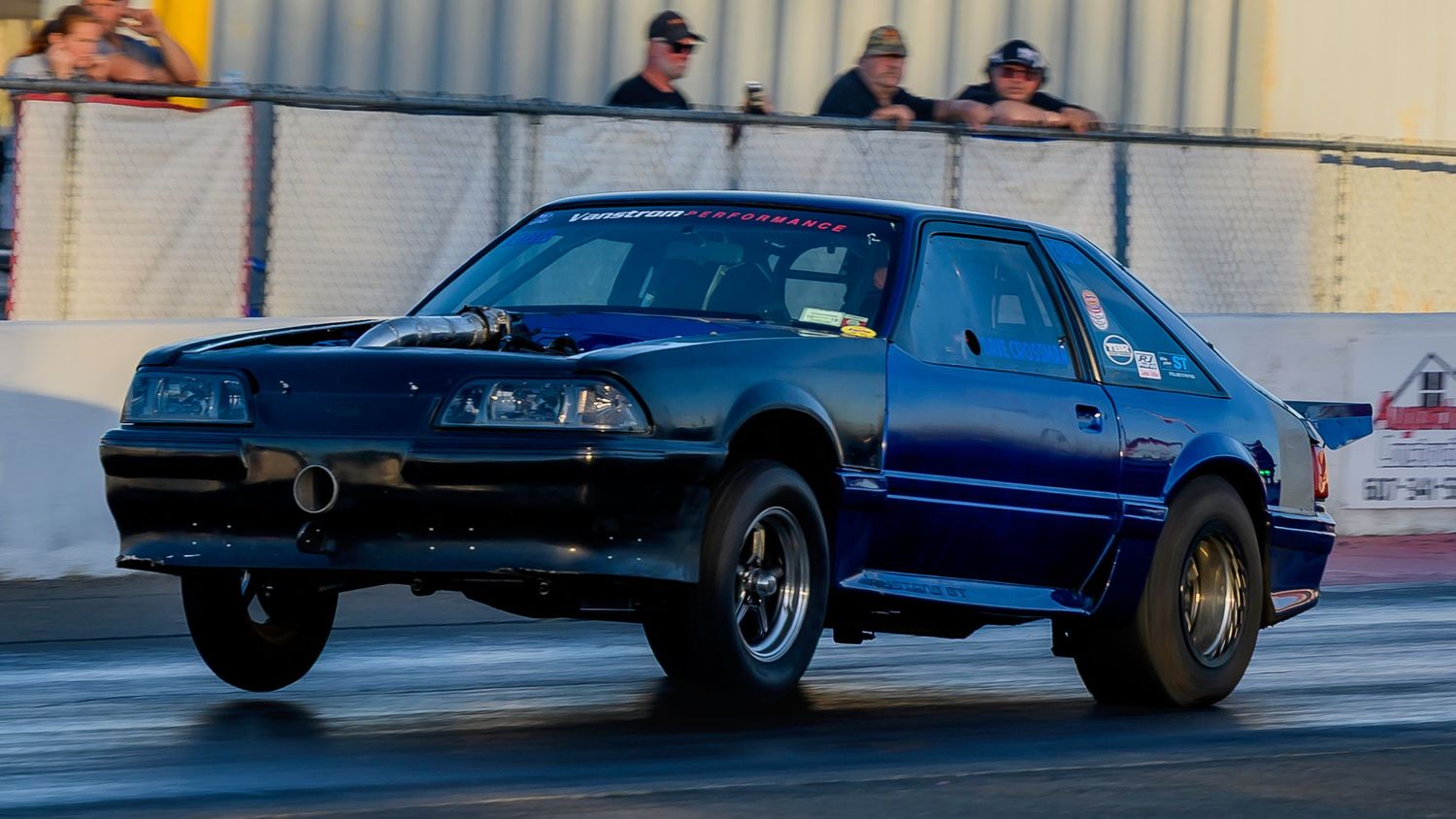 High-performance cars racing down a drag strip with spectators watching from the sidelines.