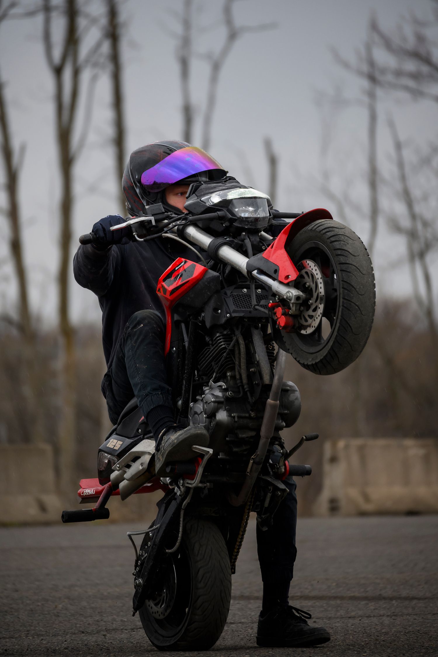 Motorcyclist performing a wheelie stunt on a black and red bike while wearing a helmet with purple visor.