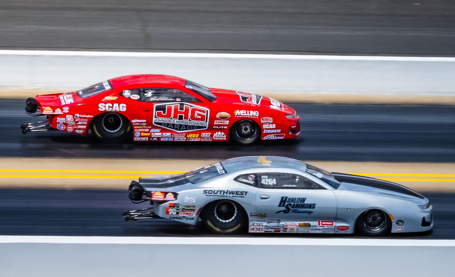 Pro stock drag racing cars racing side by side down the dragstrip at high speeds.