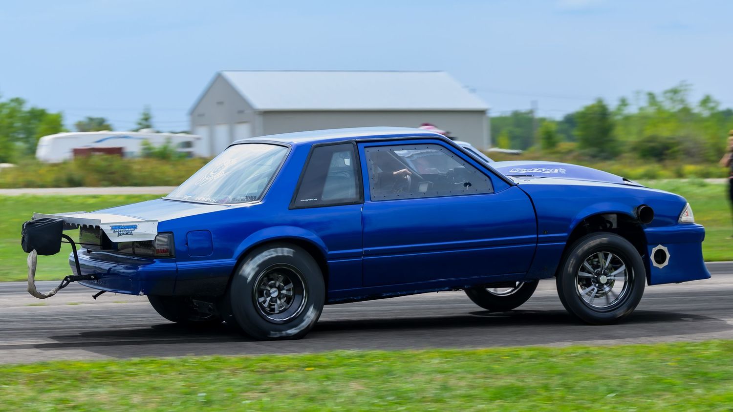 A blue drag racing car lifting its front wheels during a race on a track.