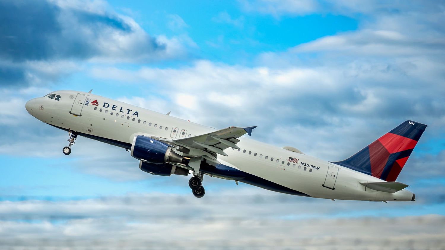 Delta Air Lines Airbus A320 aircraft climbing through partly cloudy blue sky after takeoff.