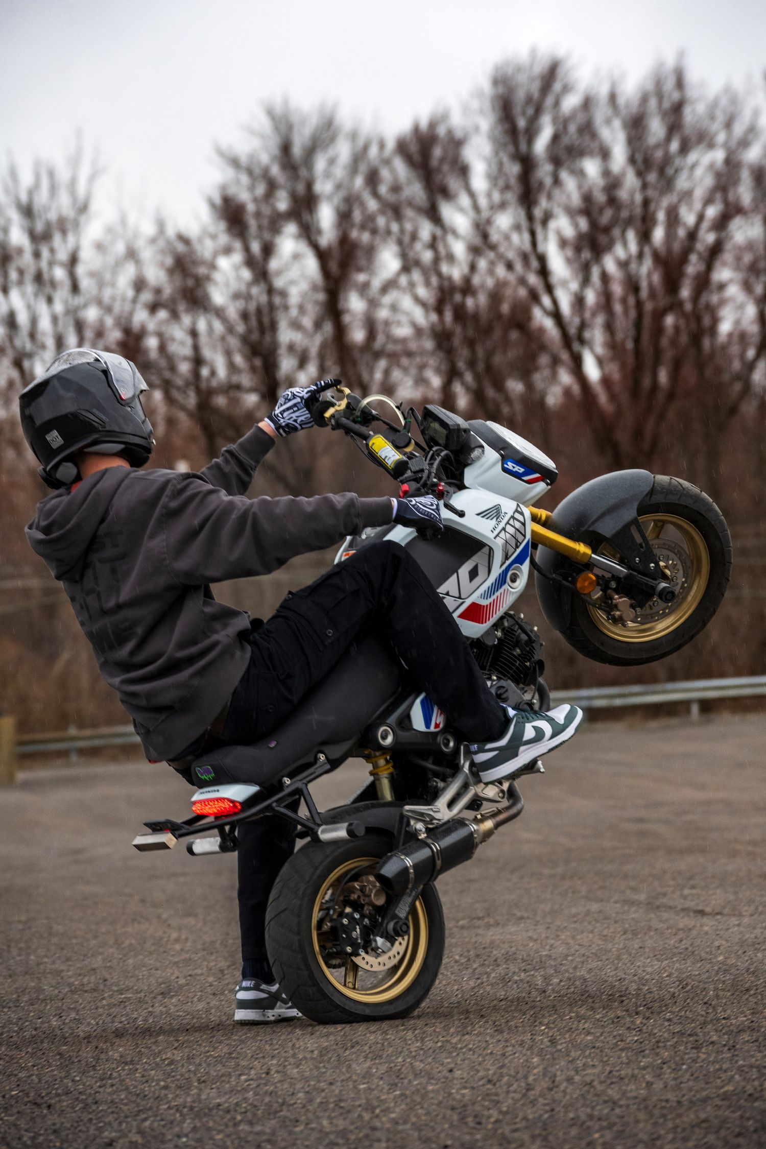 Motorcyclist performing a wheelie stunt on a sport bike with gold rims on an empty parking lot.