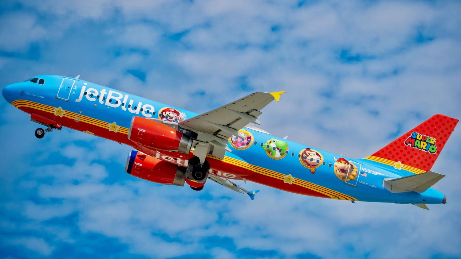 JetBlue Airways colorful Nickelodeon themed aircraft flying against a blue cloudy sky.