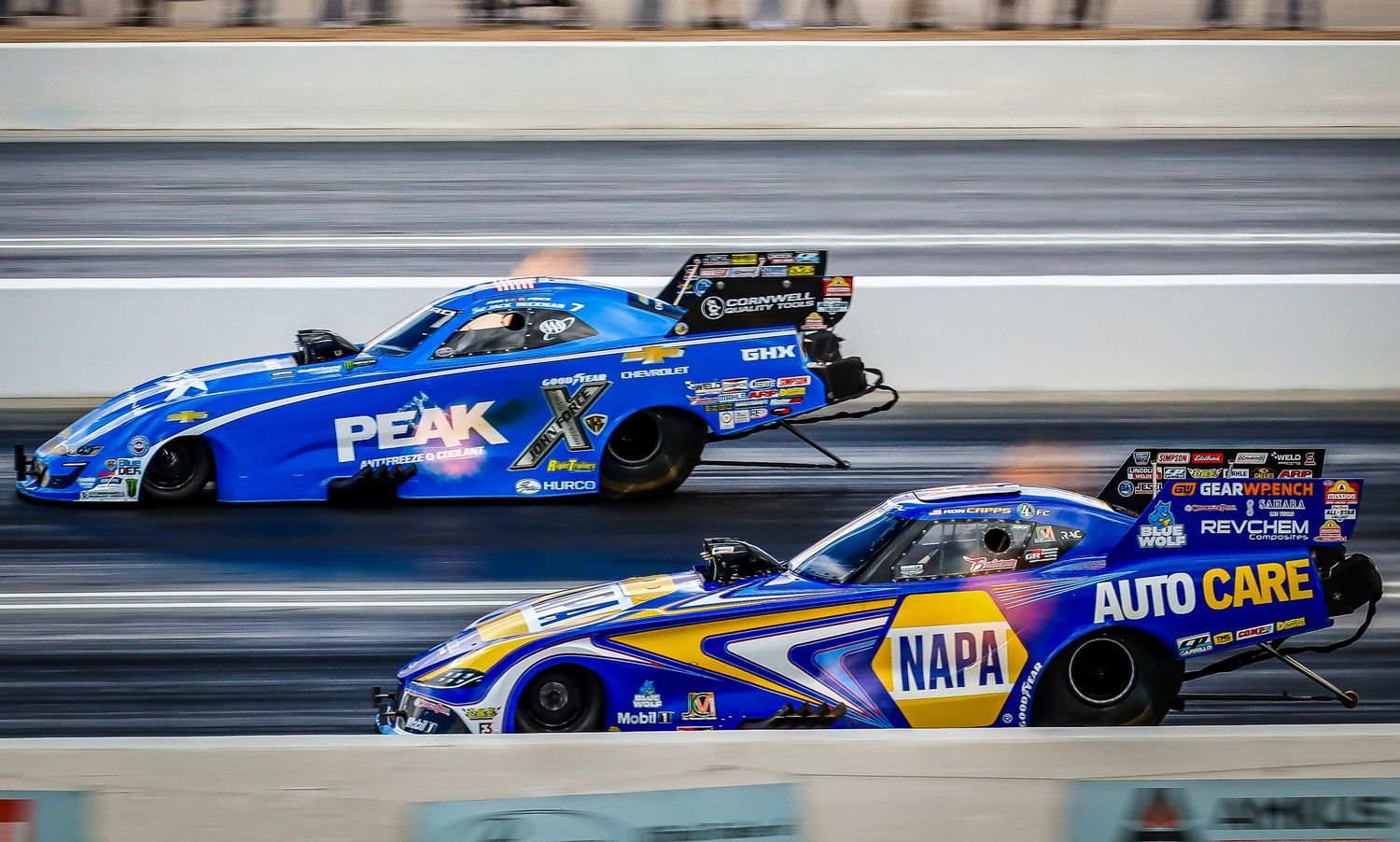 Blue dragster racing cars speeding down the track during a competitive race.