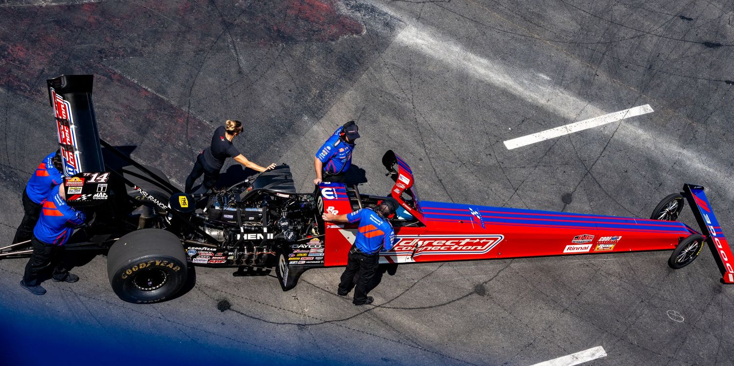 Overhead shot of racing teams and vehicles preparing on a marked track surface.