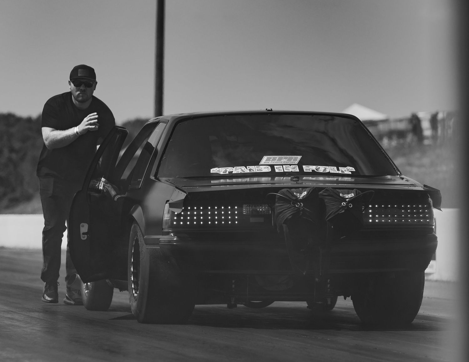 Silhouetted view of racing crew members working on classic cars in low light conditions.