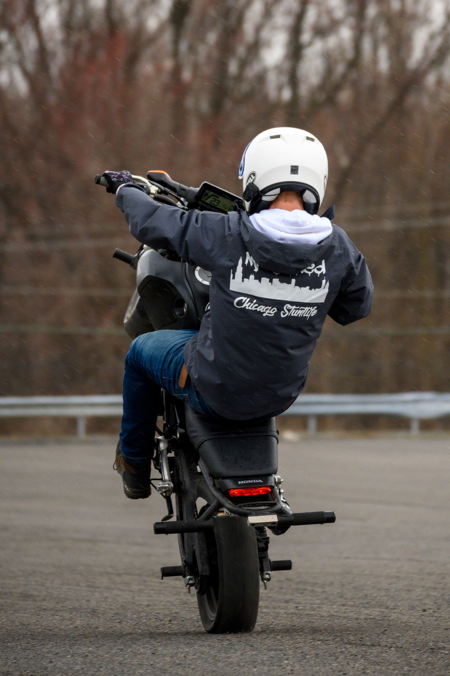Motorcyclist performing a wheelie stunt in a parking lot, wearing a white helmet and Chicago Stunts hoodie.
