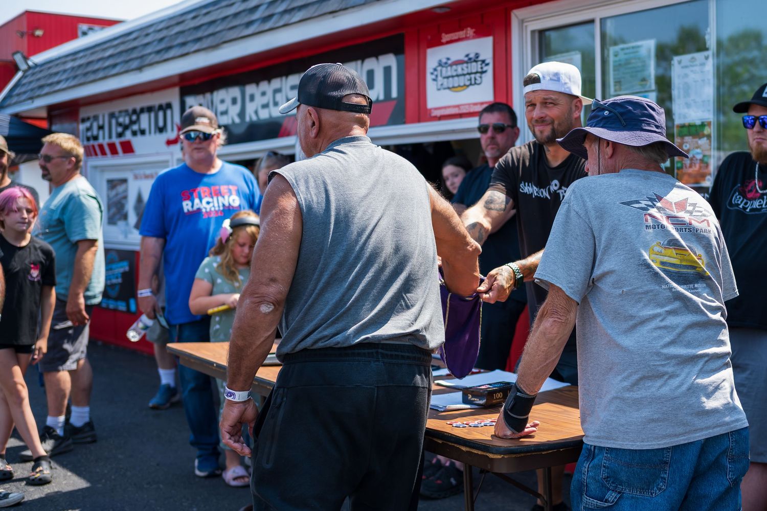 Crowd of spectators gathered outside red and white building at motorsports event.