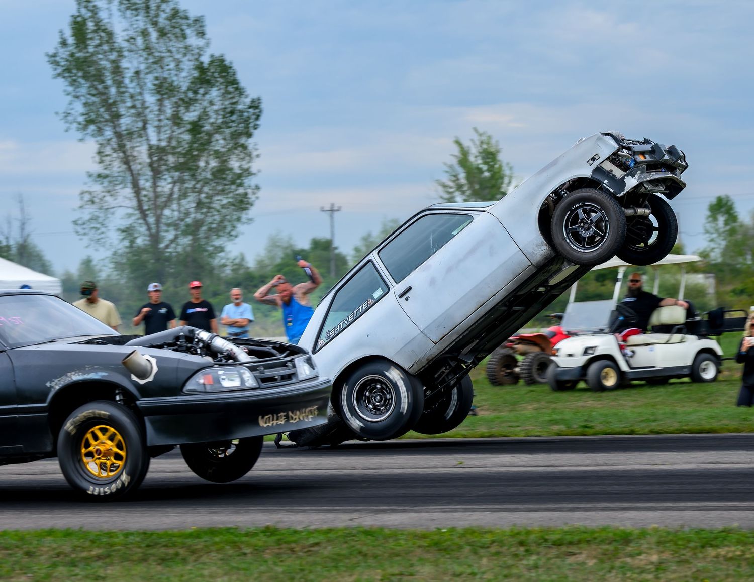 A dramatic car stunt showing one vehicle launching into the air over another during an automotive event.