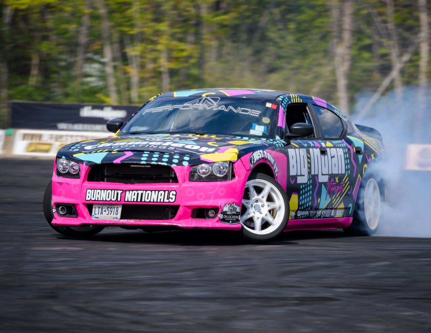 Pink Dodge Charger drift car with Burnout Nationals livery smoking tires on a race track.