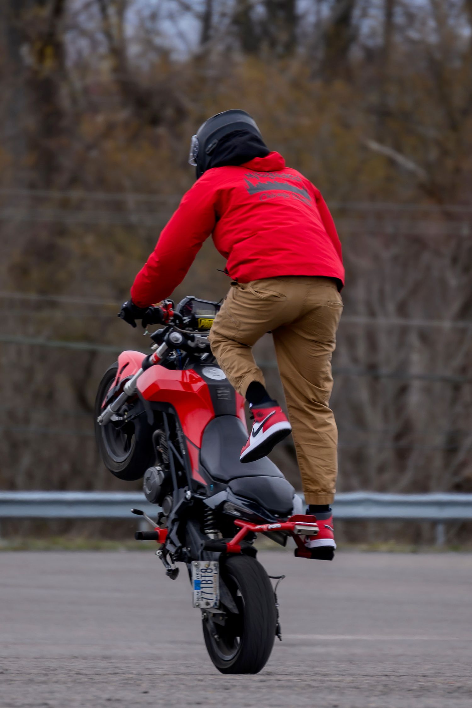 Motorcyclist performing a wheelie stunt on a red motorcycle while wearing a red jacket, tan pants, and helmet.