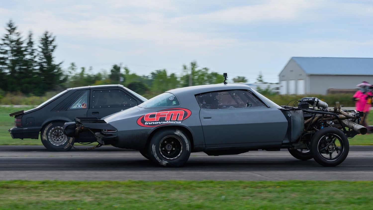 Row of high-performance cars racing down a dragstrip under blue skies.