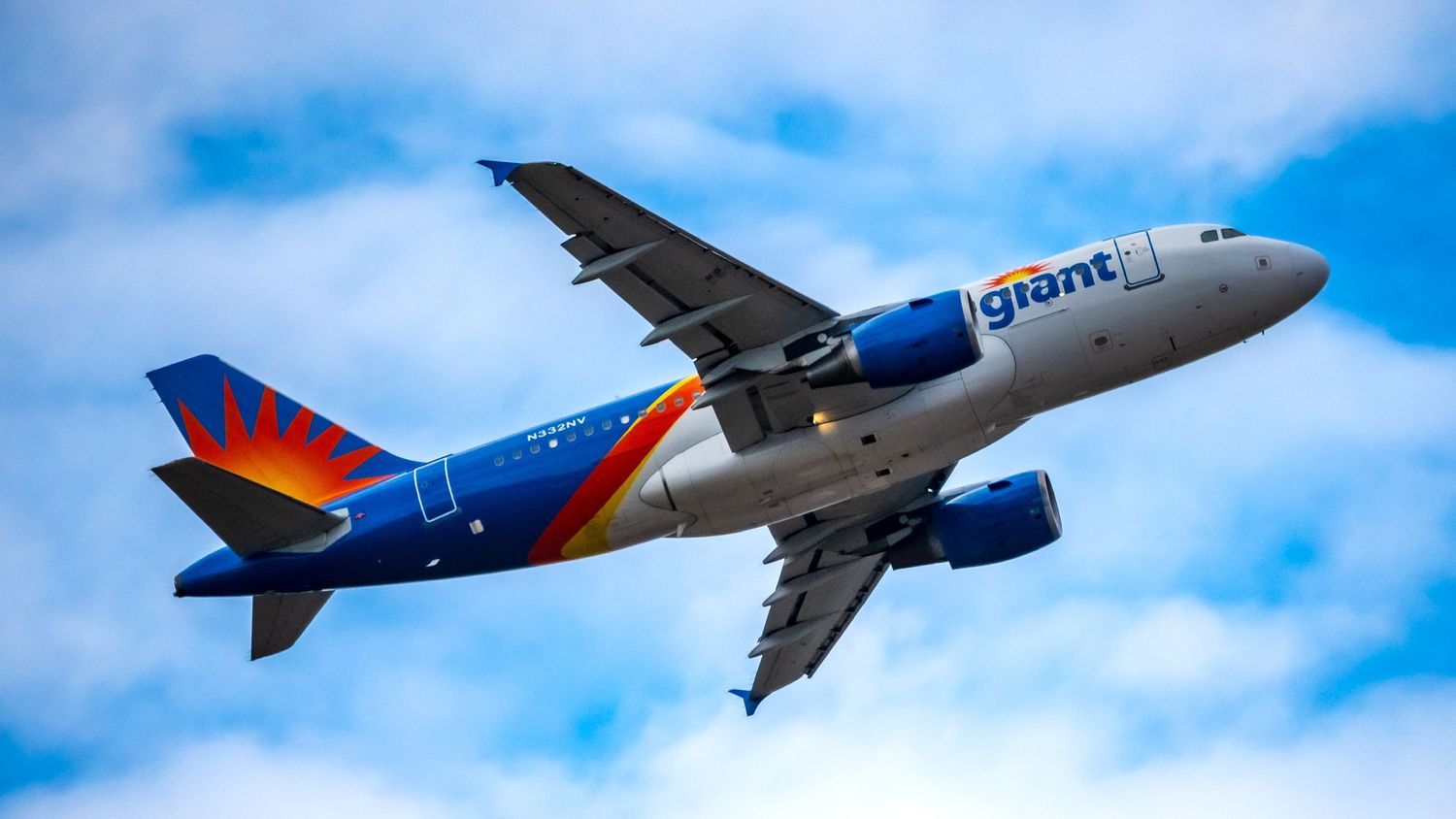 Allegiant Air giant branded Airbus A319 aircraft flying against a partly cloudy blue sky.