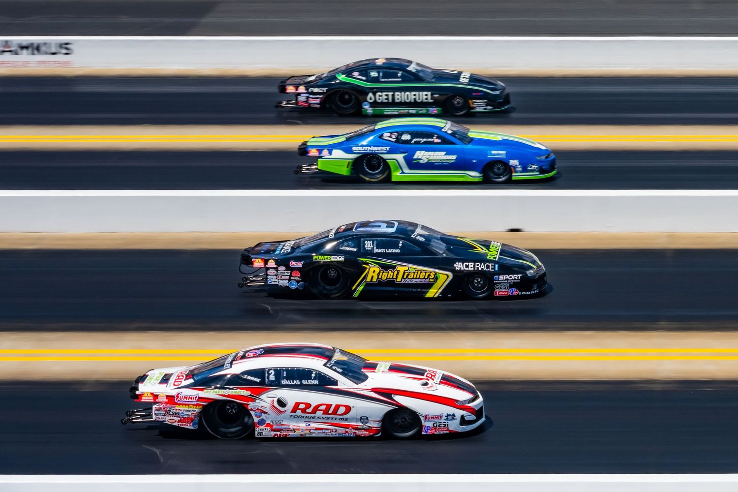 Professional drag racing competition with multiple cars racing on a sunny track.