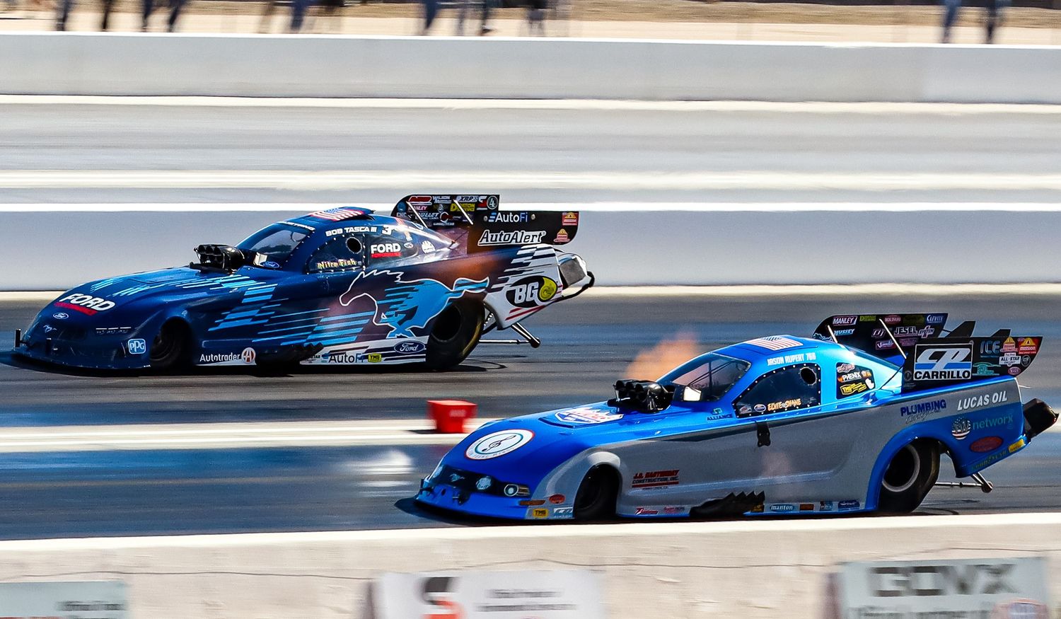Blue and red drag racing cars competing in a high-speed race event.