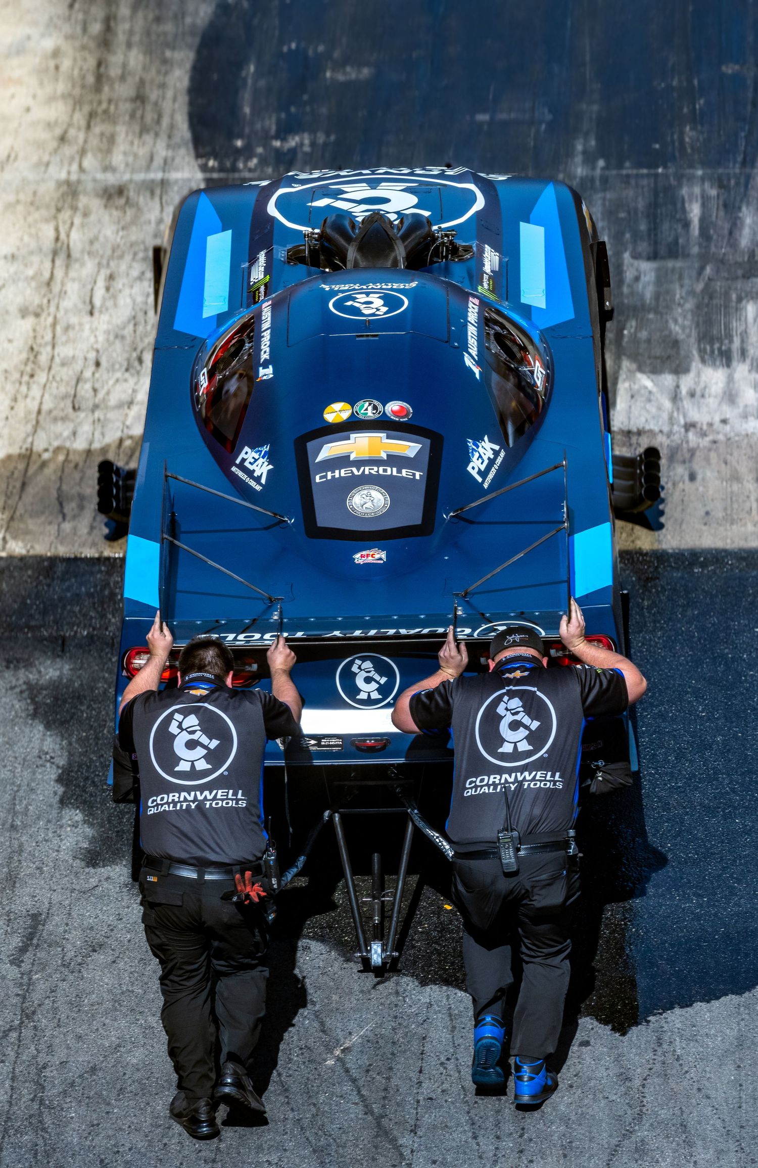 Overhead view of two crew members pushing a blue dragster on a racetrack.
