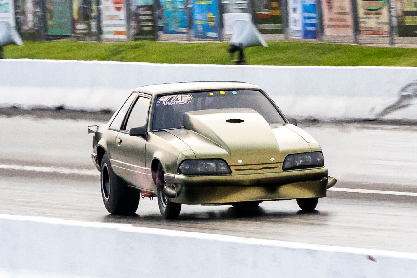 Gold drag racing car speeds down the track with motion blur in the background.