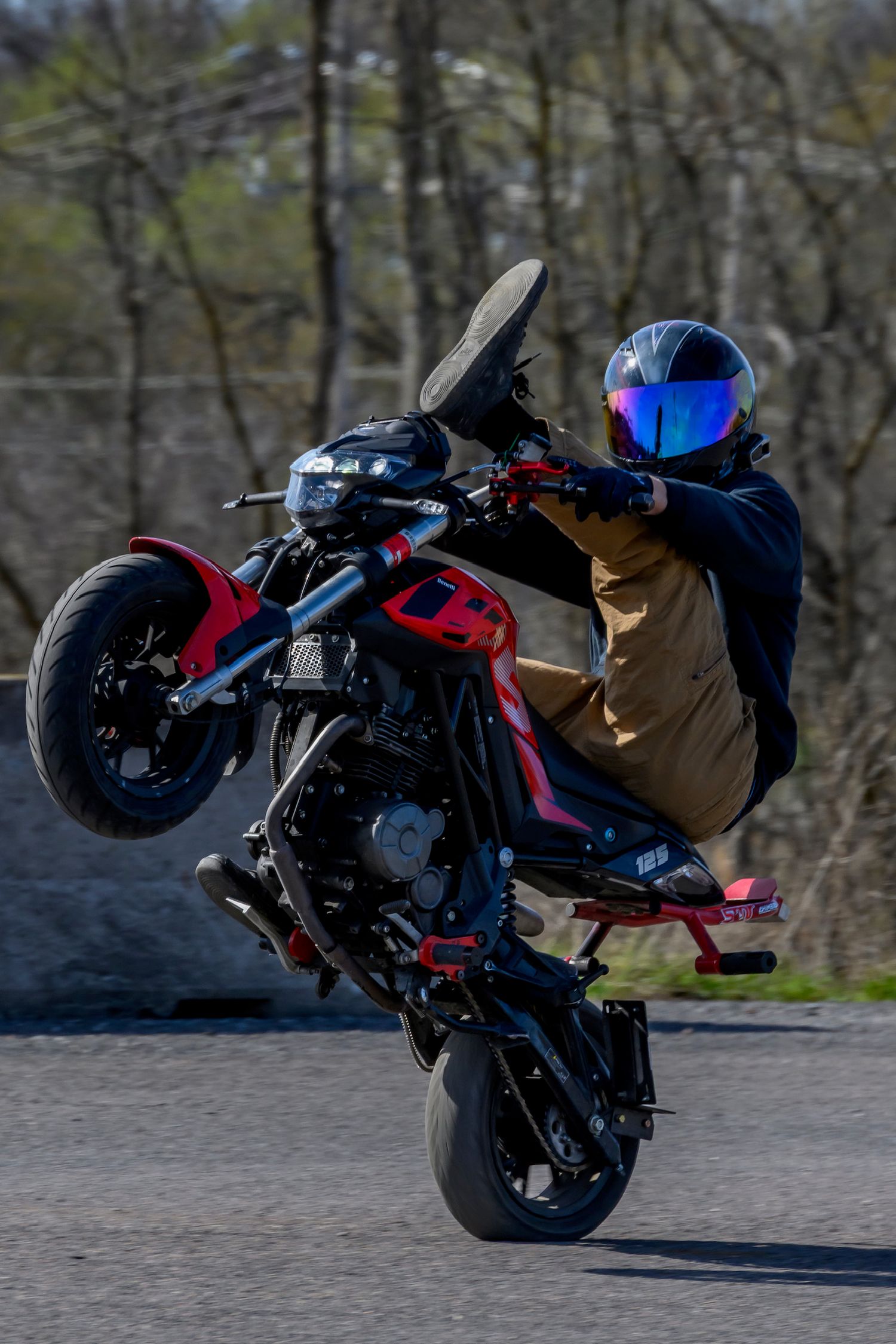 Motorcyclist performing a wheelie stunt on a red and black bike while wearing a blue iridescent helmet.