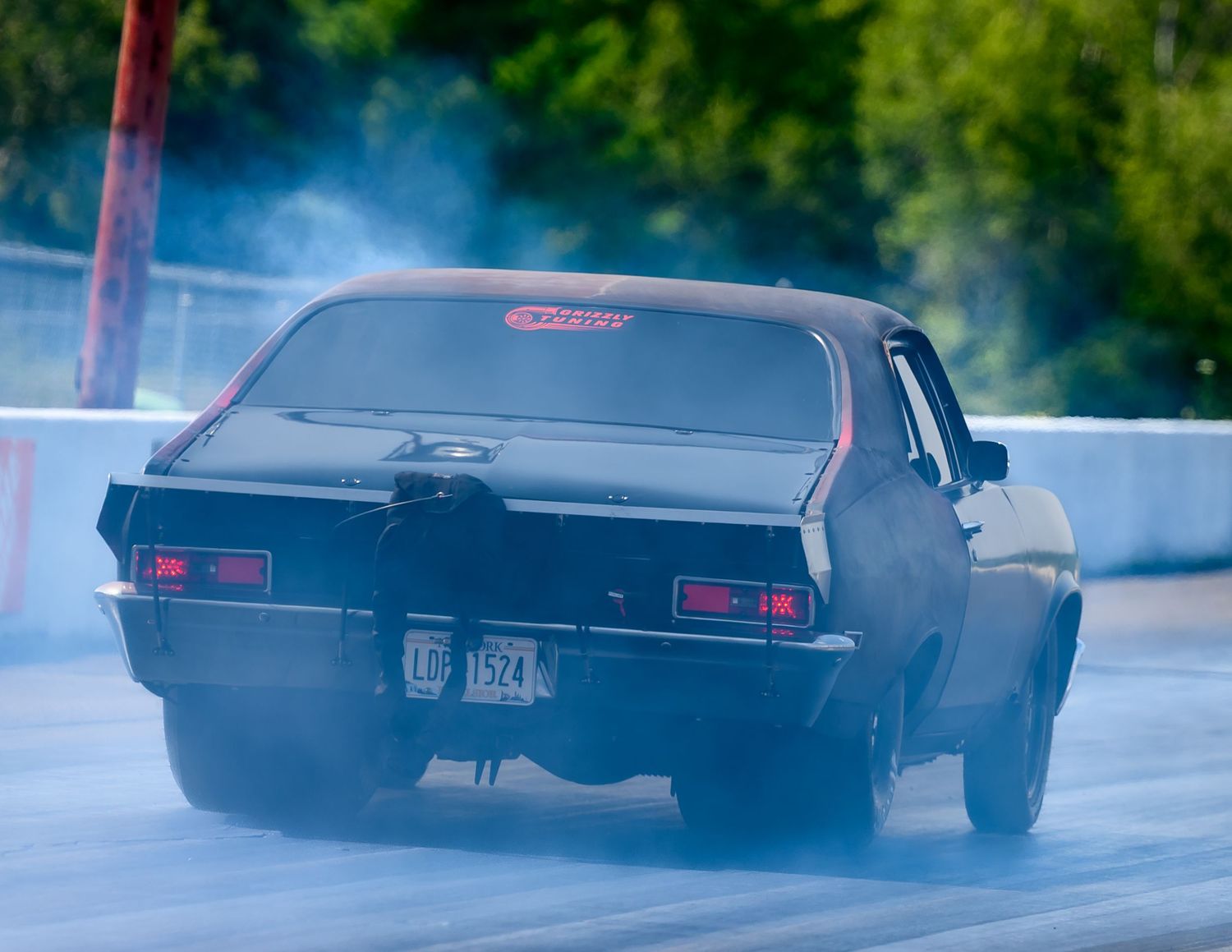 Black classic car drifting on pavement creating tire smoke during performance driving demonstration.