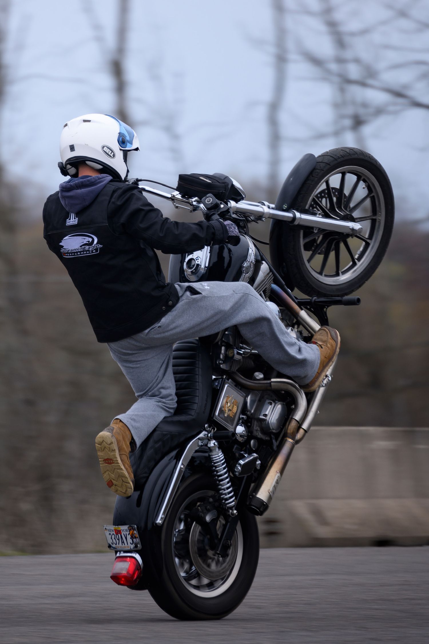 Motorcyclist performing a wheelie stunt on a custom bike while wearing a white helmet and black hoodie.