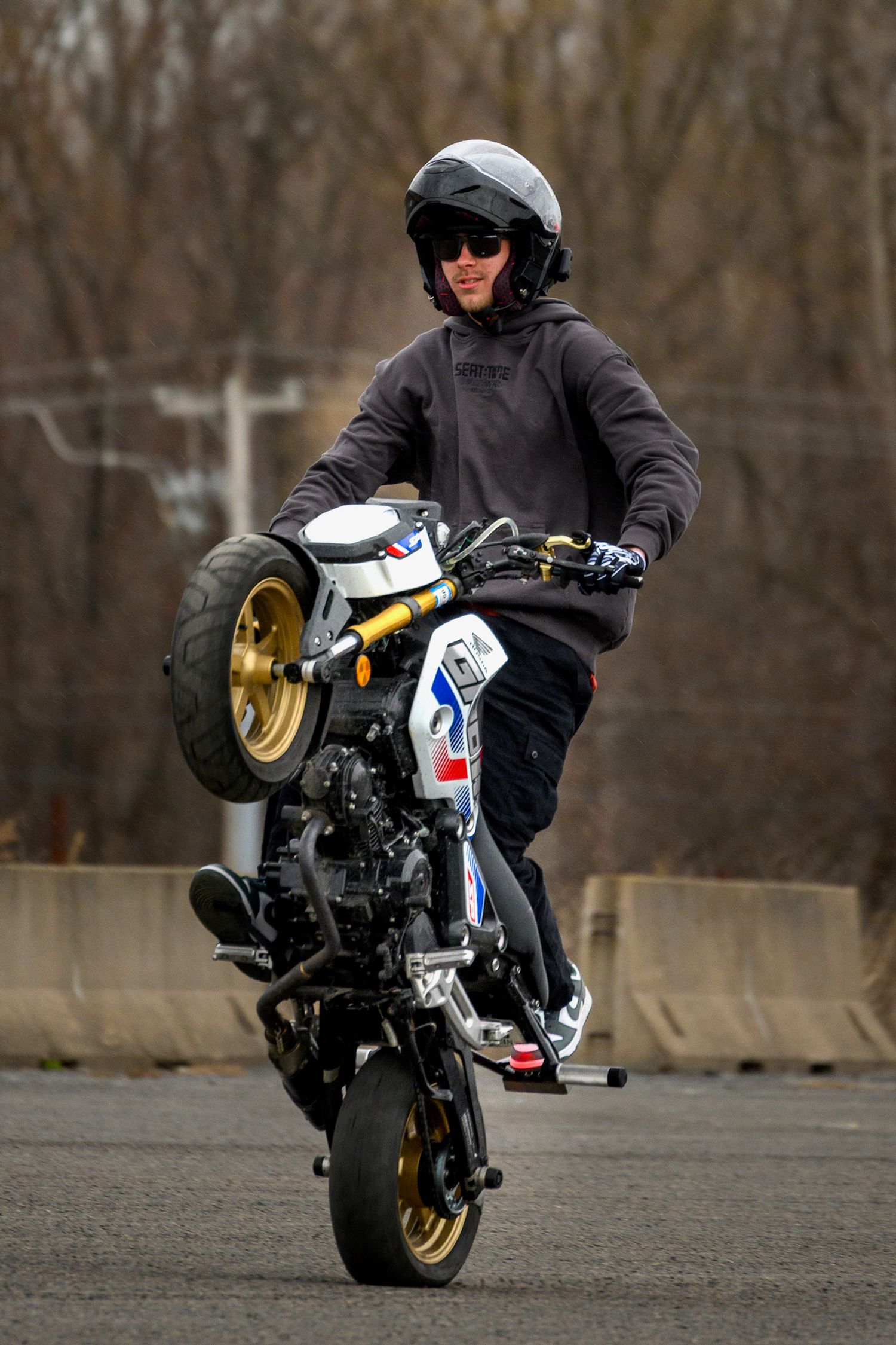 Motorcyclist performing a wheelie stunt on a custom sport bike while wearing a helmet and dark riding gear.
