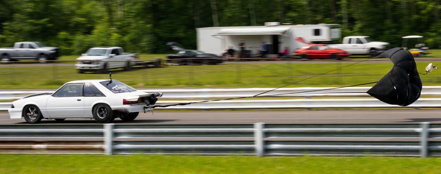 A silver car racing on a track with a white guardrail in the background.