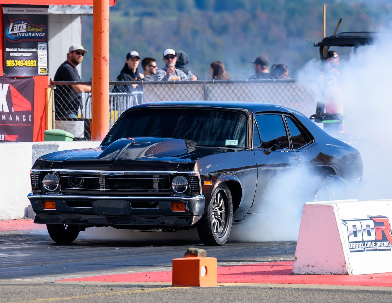 Drag racing cars creating burnout smoke on the starting line of a race track.