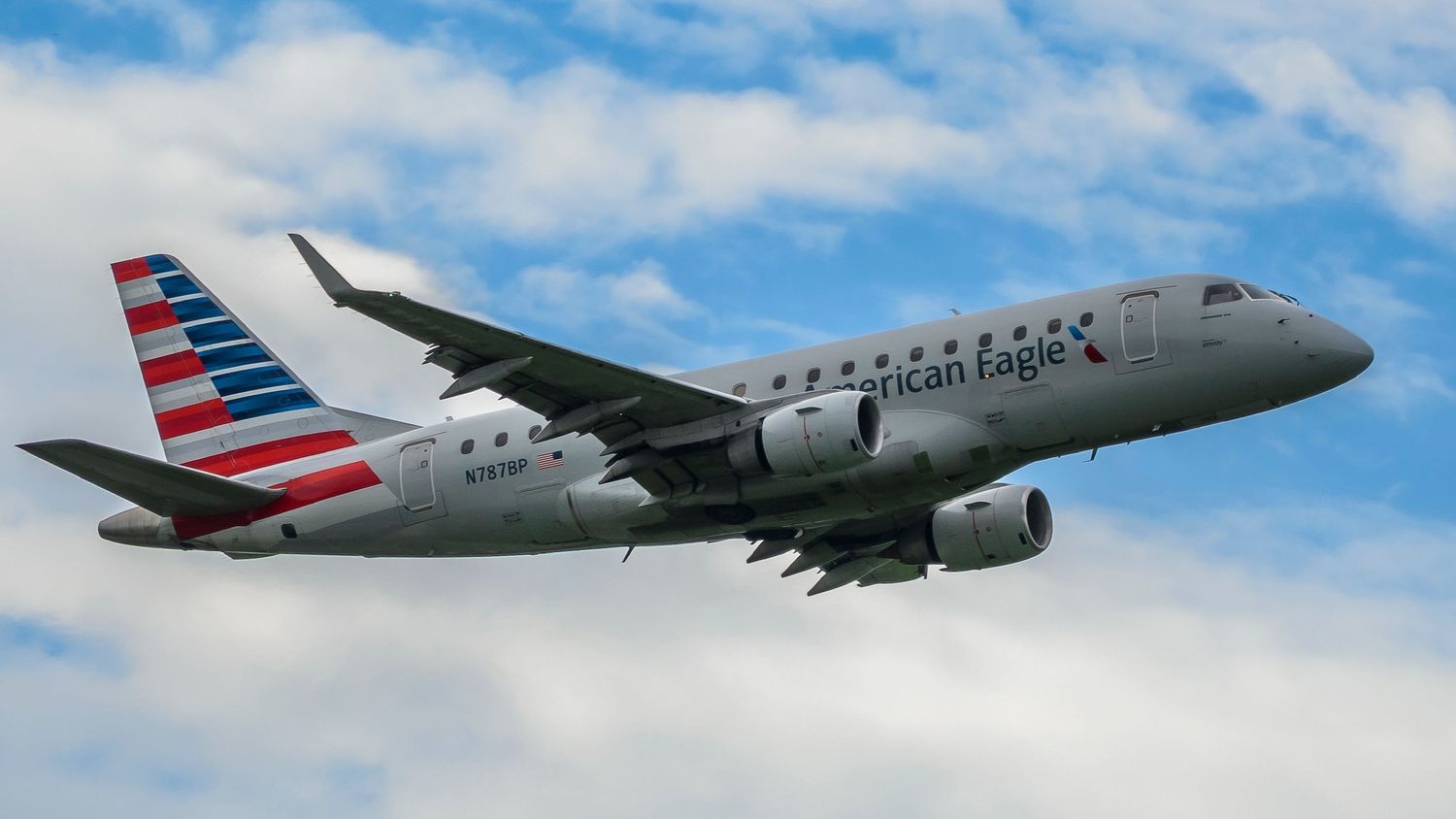 American Eagle Embraer E175 regional jet aircraft in flight against a partly cloudy blue sky.
