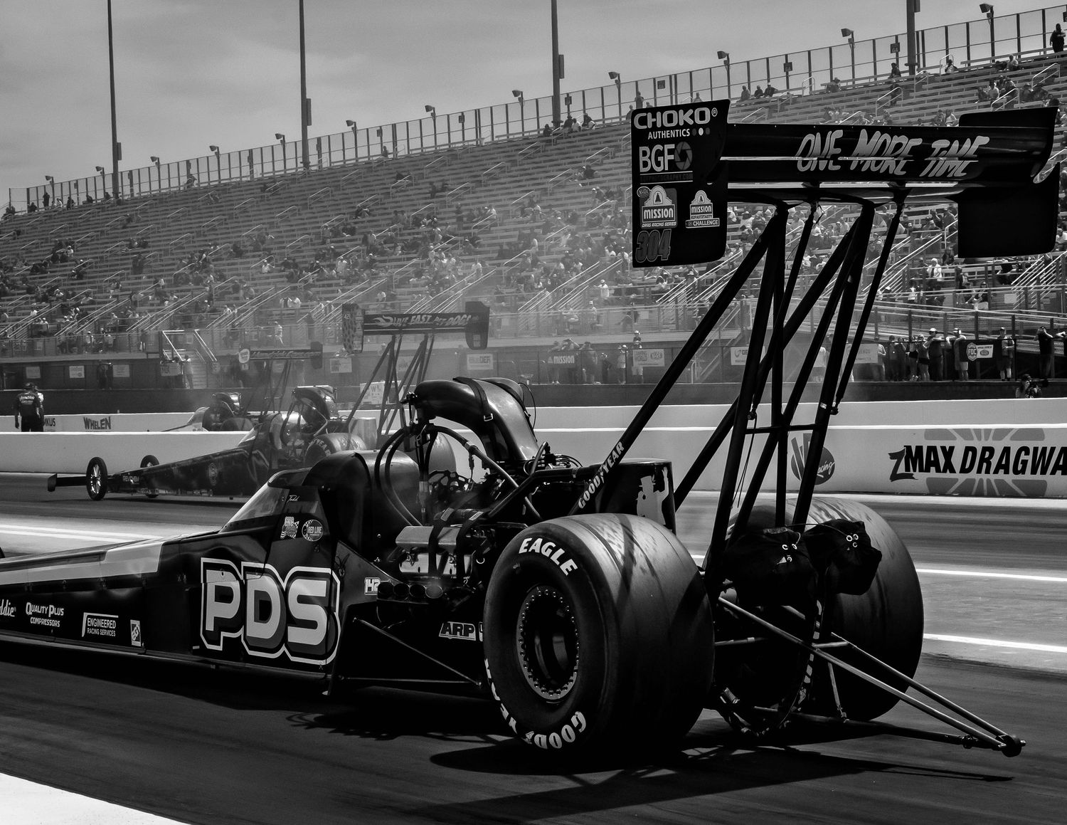 Black and white photo of drag racing cars lined up at a professional racing event.