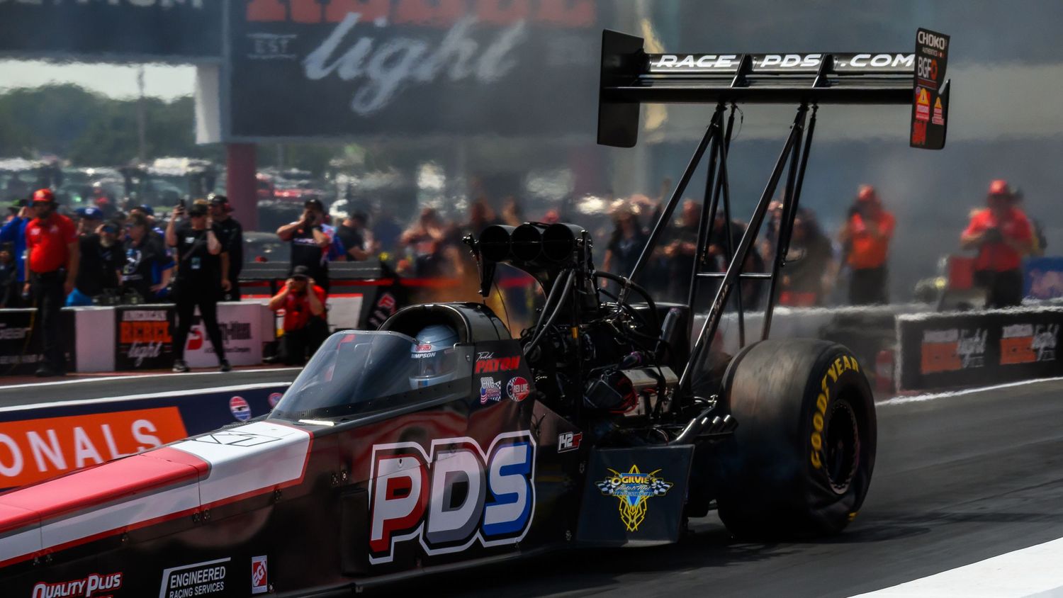 Blurred drag racing action shot showing multiple vehicles on the track during competition.