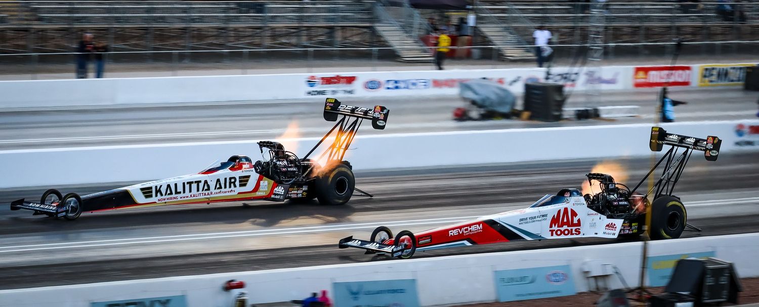 Drag racing cars competing on a professional racetrack with smoke and speed effects.