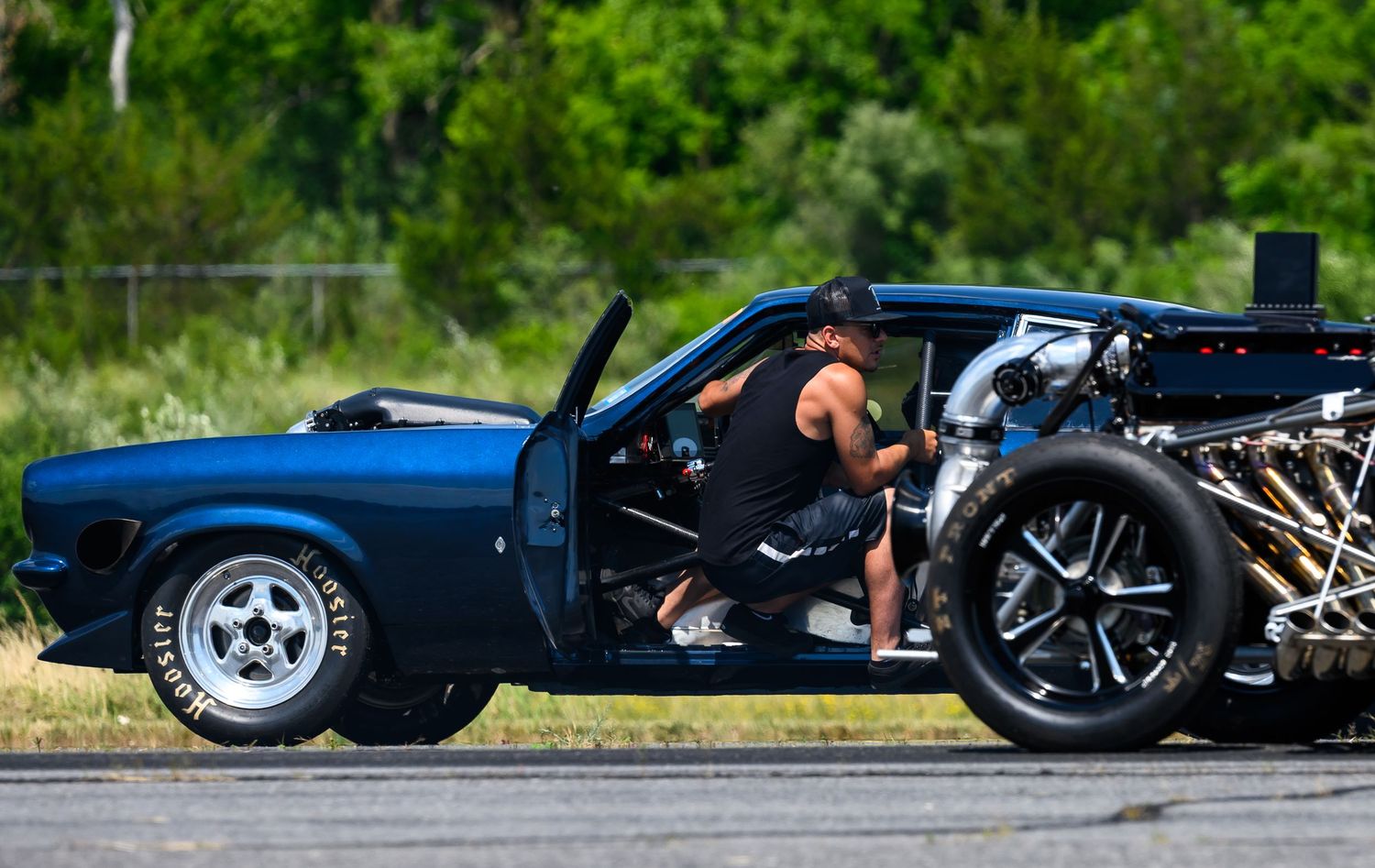 A blue classic muscle car with exposed engine components being prepared for racing.