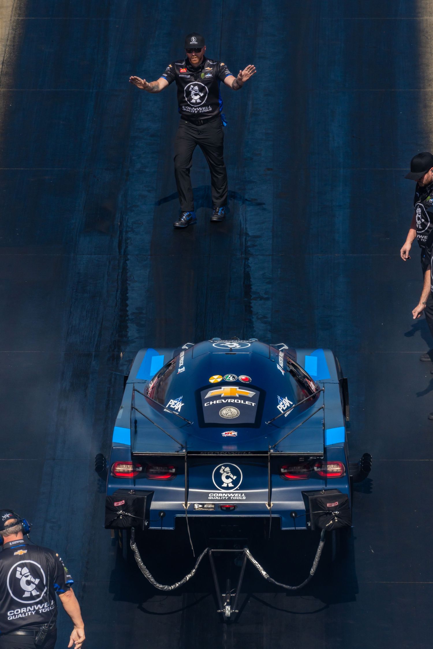 Aerial view of a dark blue race car being prepared by crew members on track.