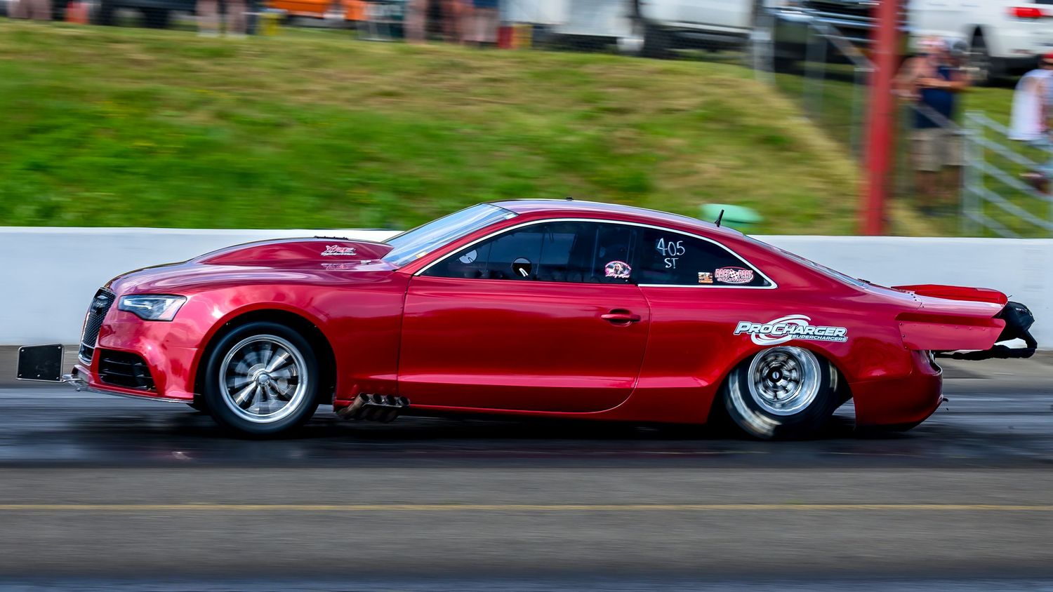 Red performance cars line up on a racing track during a drag racing event.