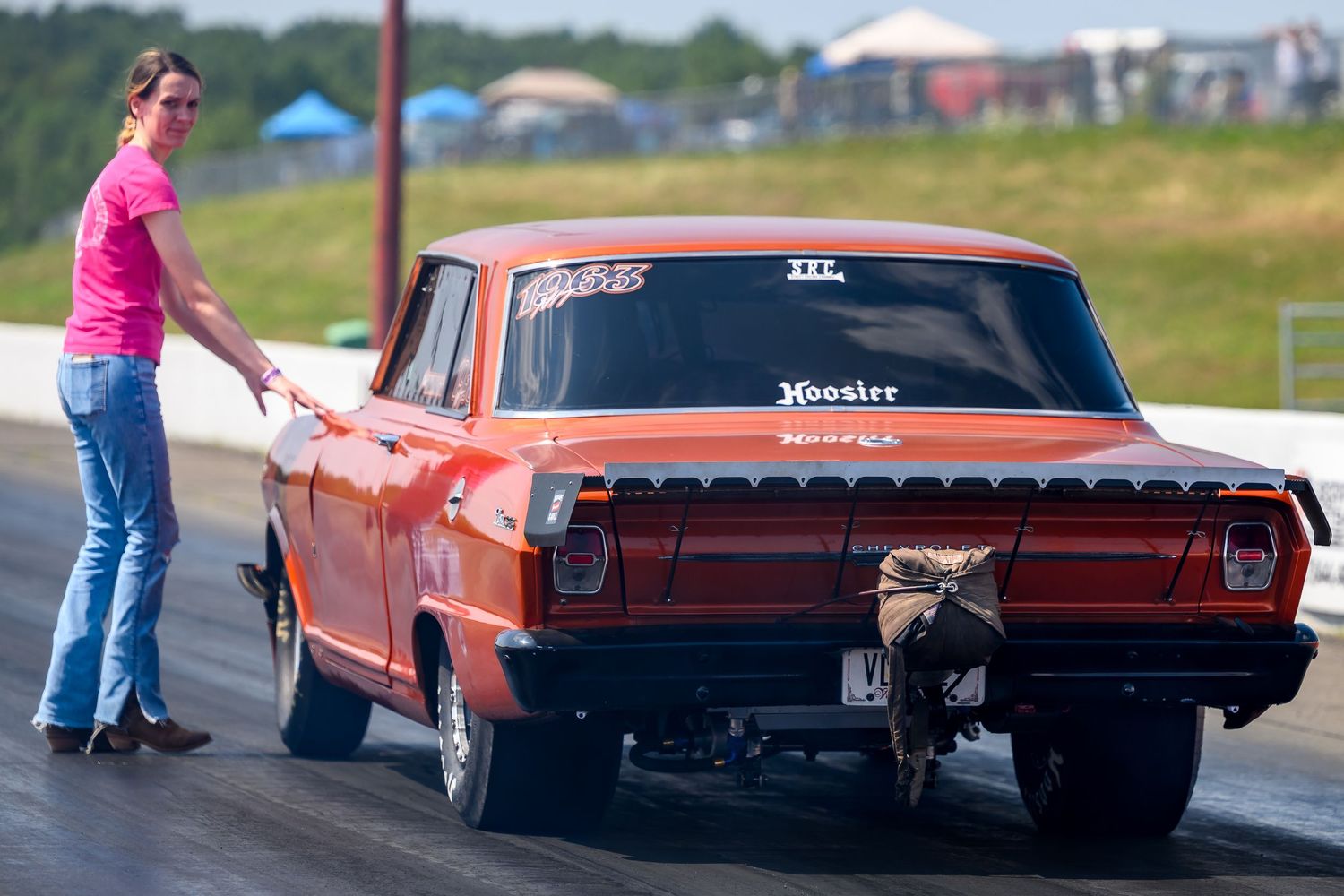 Classic red muscle cars lined up at a drag racing event on a sunny day.