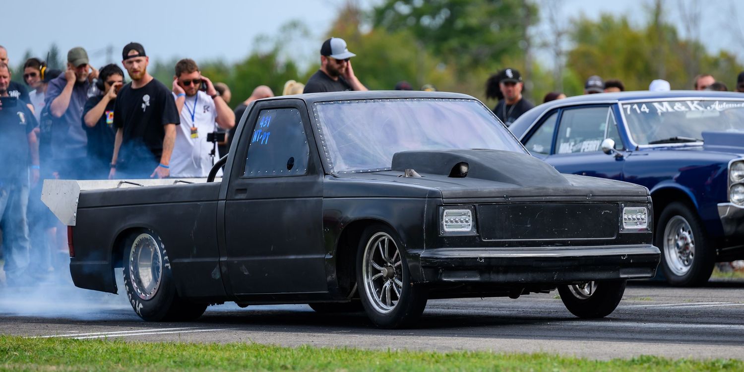 A black lowered pickup truck performing a burnout at a drag racing event.