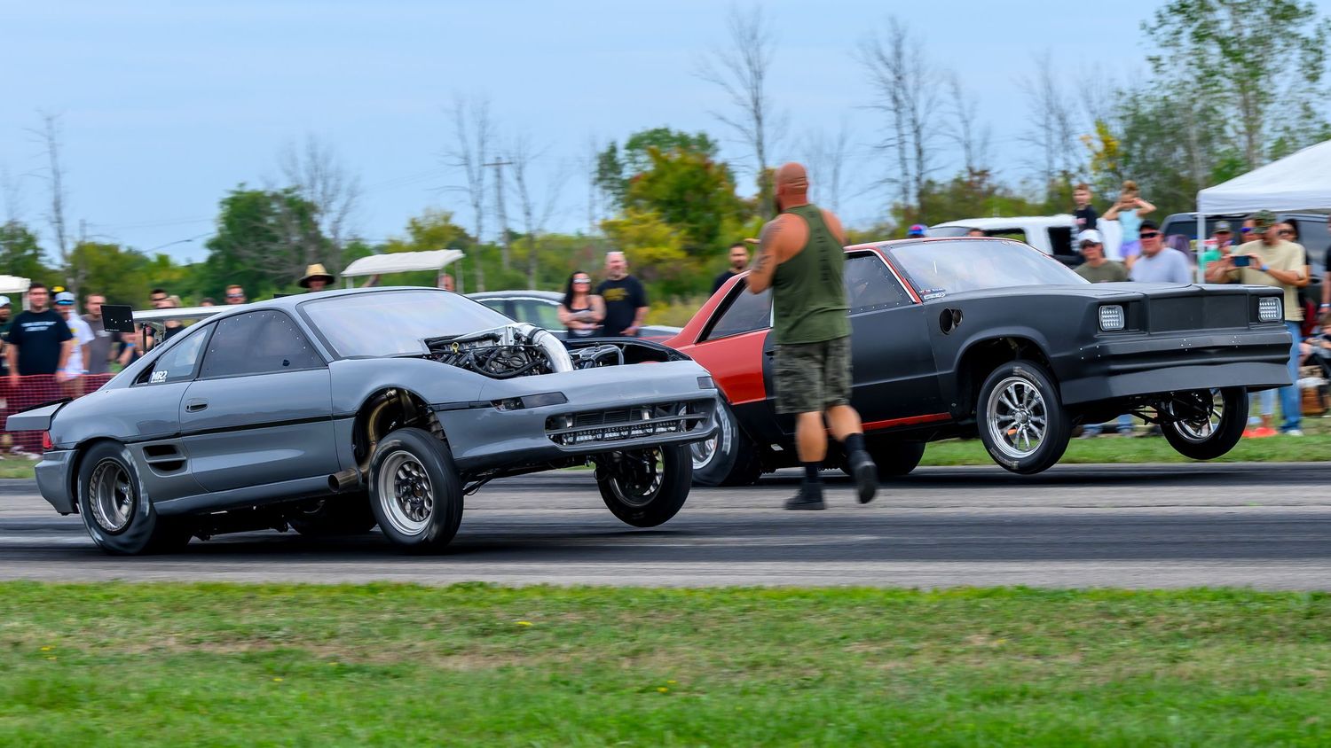 Wide shot of classic cars lined up at an outdoor motorsport event.
