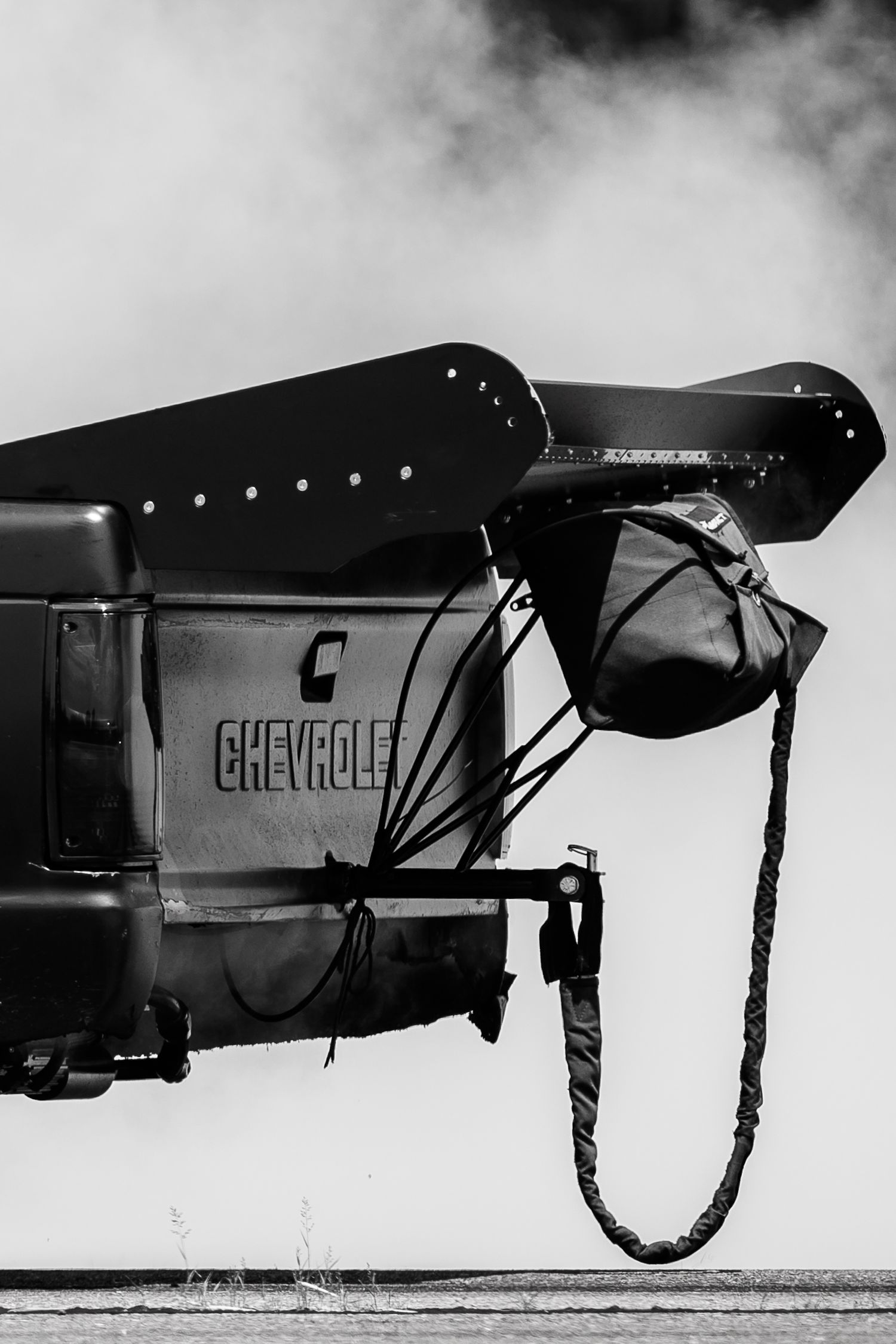 Black and white detail shot of a modified Chevrolet vehicle spoiler in smoke.
