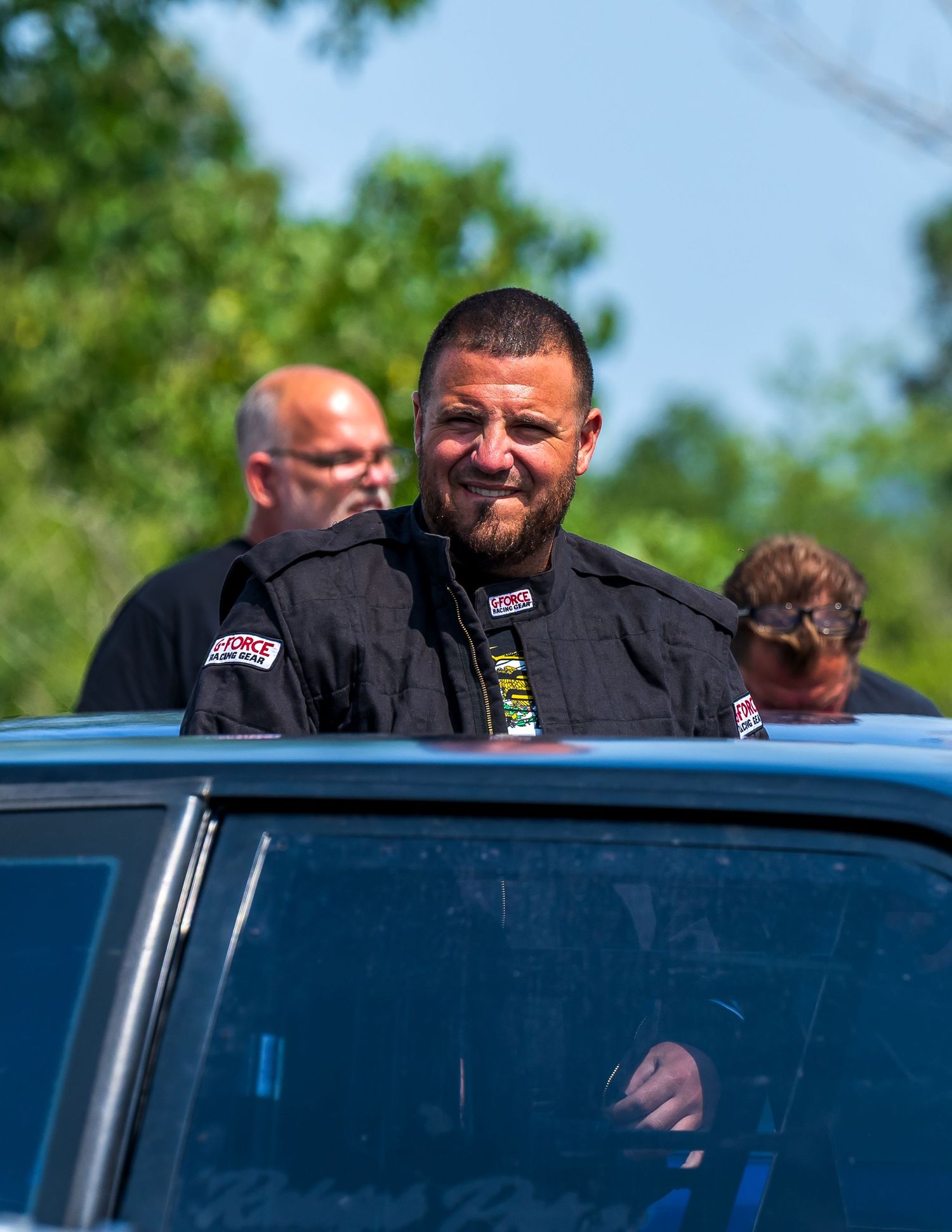 Racing crew members in black uniforms gathered around a vehicle during an event.