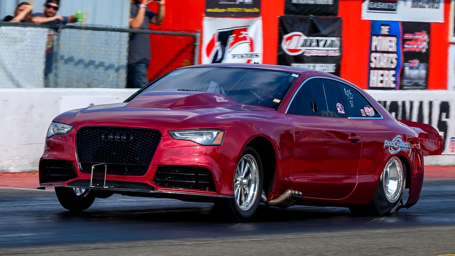 Multiple red drag racing cars compete on a professional racing strip.