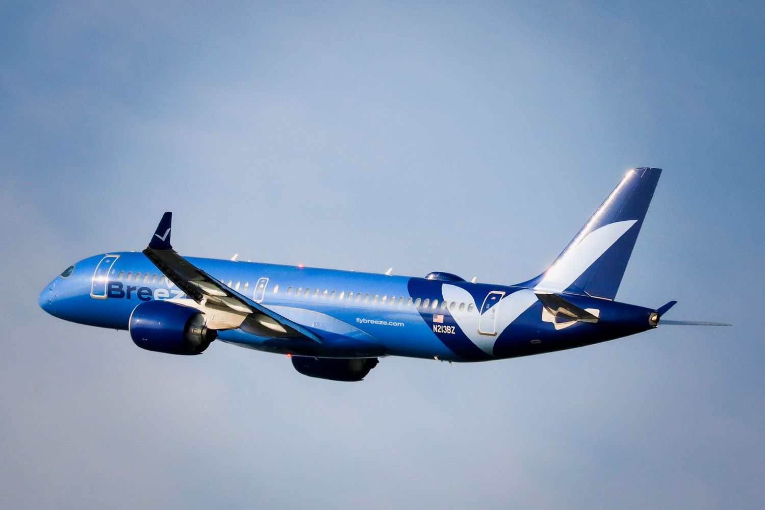 Blue Breeze Airlines Airbus A220 aircraft soaring through partly cloudy skies during flight.