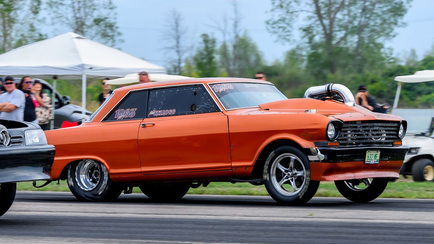 Orange and black classic cars racing side by side on a dragstrip.