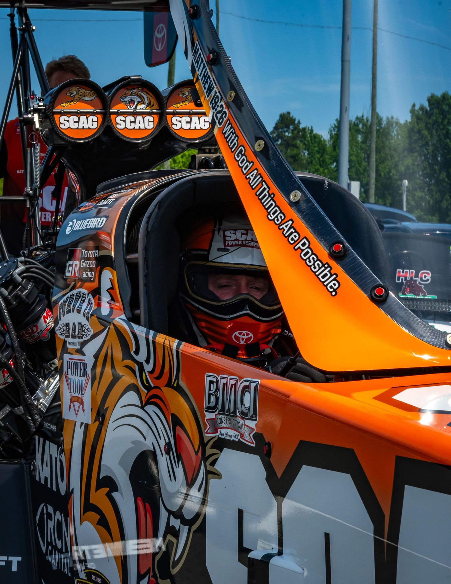 Orange and white race car details showing custom decals and sponsor logos against a blue sky background.
