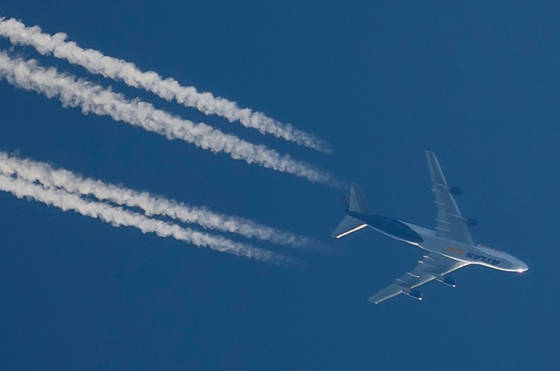 Large commercial airplane flying high in blue sky leaving four white contrails in its wake.